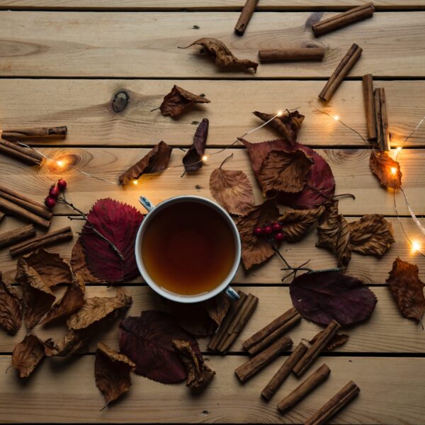 A cup of brown tea surrounded by cinnamon sticks and a few lights.