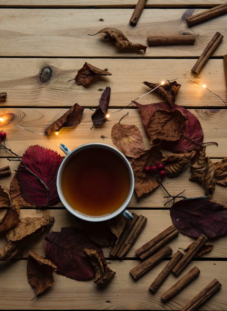 A cup of brown tea surrounded by cinnamon sticks and a few lights.