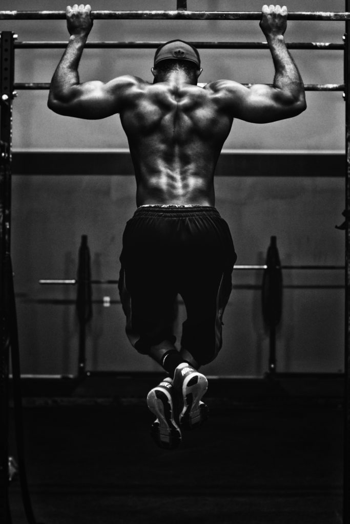 BLACK AND WHITE PHOTO OF MUSCULAR MAN DOING PULL UP FROM BEHIND
